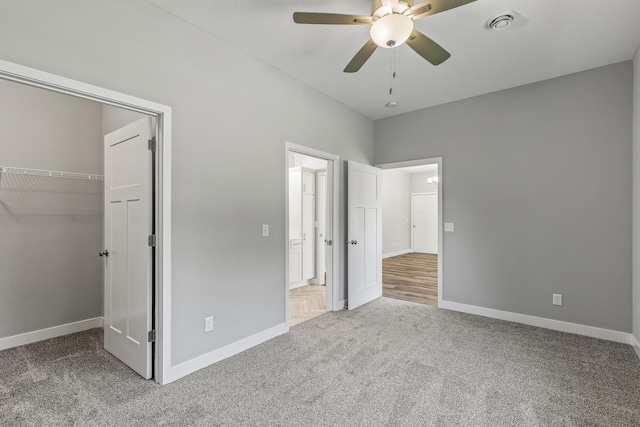 unfurnished bedroom featuring a closet, carpet flooring, a walk in closet, and baseboards