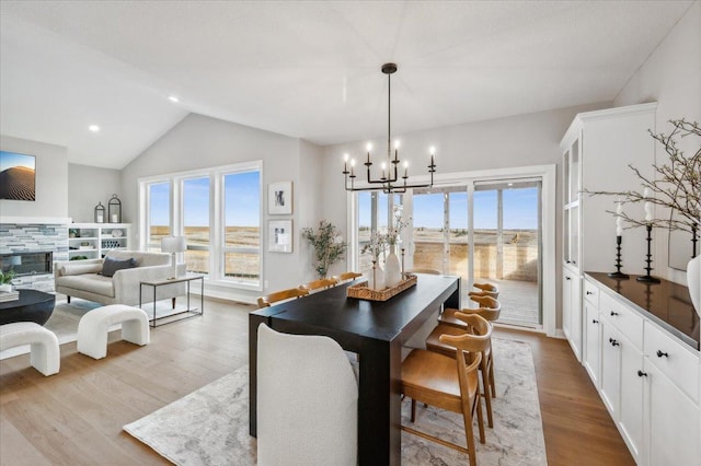 dining space featuring a stone fireplace, recessed lighting, a notable chandelier, wood finished floors, and vaulted ceiling