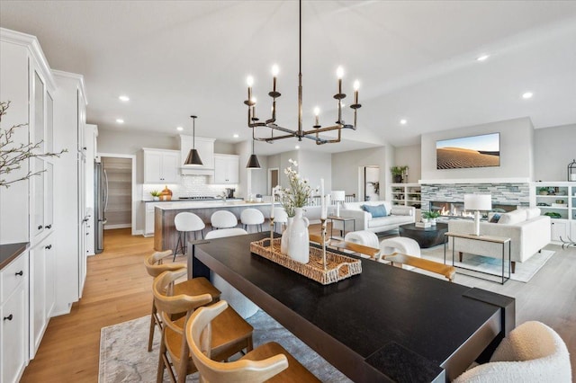 dining area with light wood-type flooring, vaulted ceiling, a stone fireplace, and recessed lighting