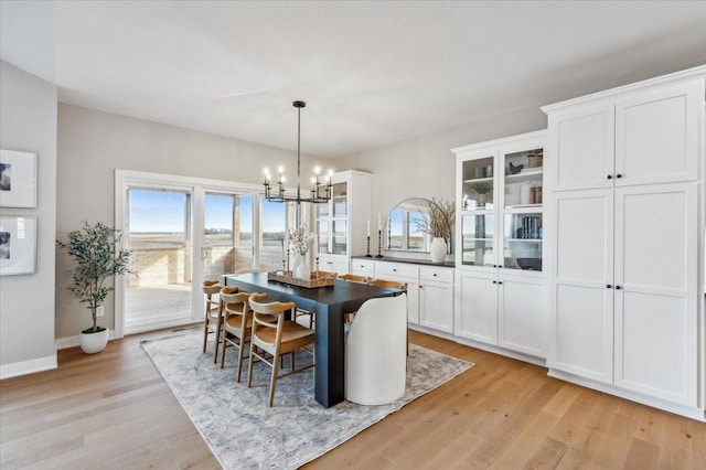 dining area featuring baseboards, light wood finished floors, and an inviting chandelier