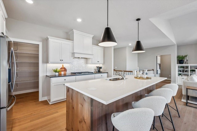 kitchen with a breakfast bar area, tasteful backsplash, light wood-style flooring, appliances with stainless steel finishes, and a sink