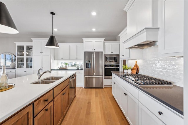 kitchen featuring stainless steel appliances, a sink, hanging light fixtures, decorative backsplash, and light wood finished floors