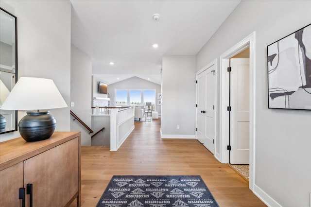 hall with light wood-type flooring, lofted ceiling, an upstairs landing, and recessed lighting