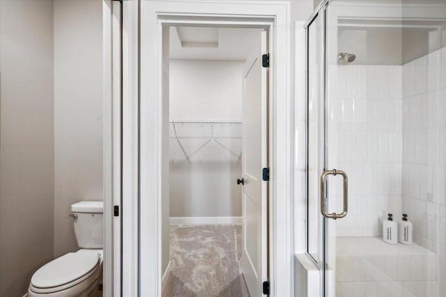 full bathroom featuring toilet, a shower stall, a walk in closet, and baseboards