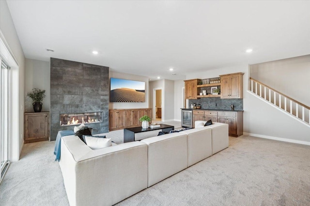 living room featuring wine cooler, a fireplace, stairway, and light colored carpet