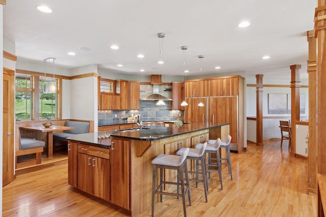 6 Black Lake Rd, North Oaks, MN 55127 - kitchen featuring wall chimney range hood, brown cabinetry, light wood finished floors, a spacious island, and decorative backsplash