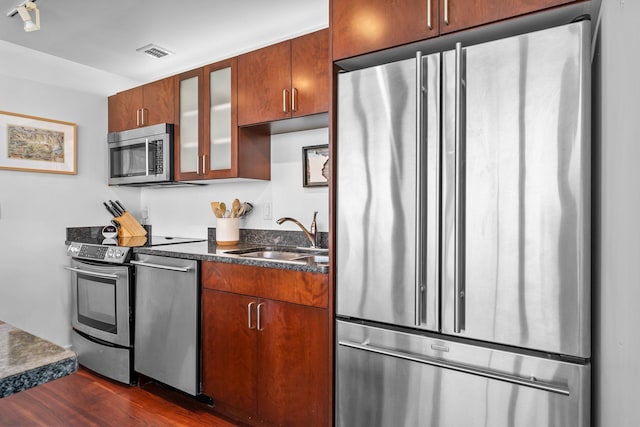 kitchen with visible vents, dark wood finished floors, a sink, stainless steel appliances, and glass insert cabinets