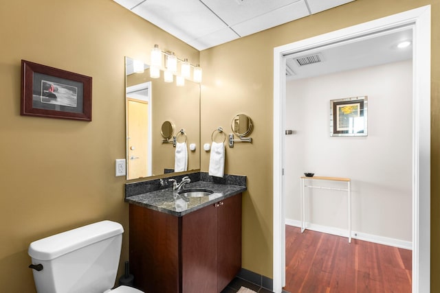 half bath featuring visible vents, baseboards, toilet, wood finished floors, and vanity