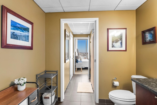 hallway featuring tile patterned floors, a drop ceiling, and baseboards