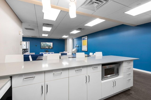 kitchen with stainless steel microwave, white cabinetry, light countertops, and visible vents