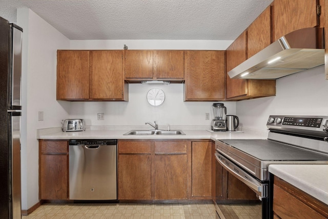 kitchen featuring under cabinet range hood, a sink, appliances with stainless steel finishes, brown cabinets, and light floors