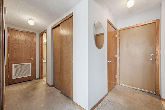 hall featuring baseboards, concrete floors, visible vents, and a textured ceiling