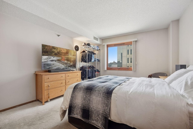 bedroom with a textured ceiling, light colored carpet, visible vents, baseboards, and a closet