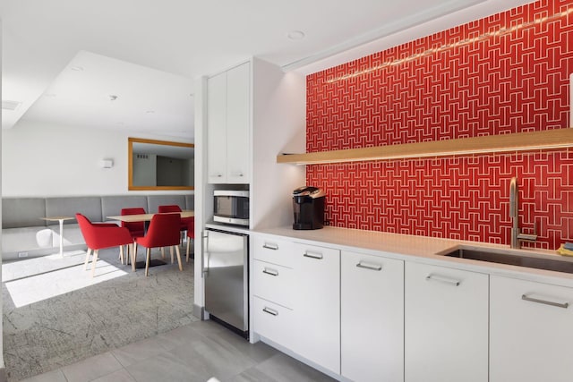 kitchen with light carpet, light tile patterned floors, stainless steel microwave, refrigerator, and a sink