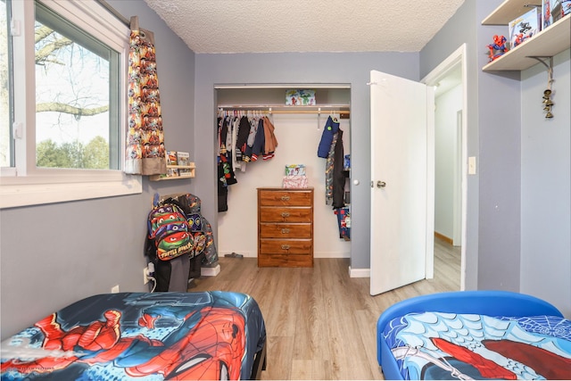 bedroom featuring a textured ceiling, a closet, wood finished floors, and baseboards