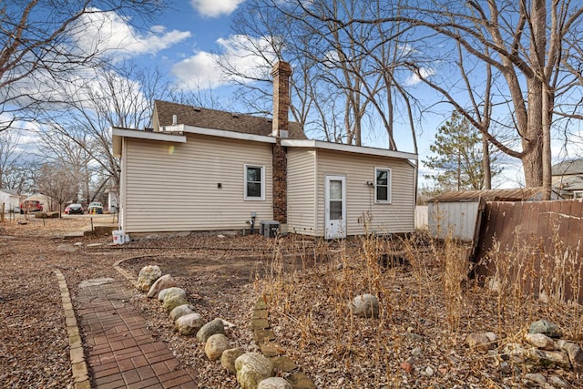 back of property featuring a shingled roof, fence, a chimney, and central AC unit