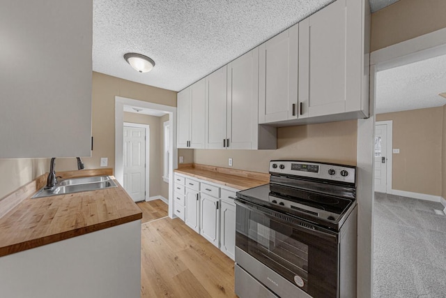 kitchen with a sink, electric range, wood counters, and white cabinetry