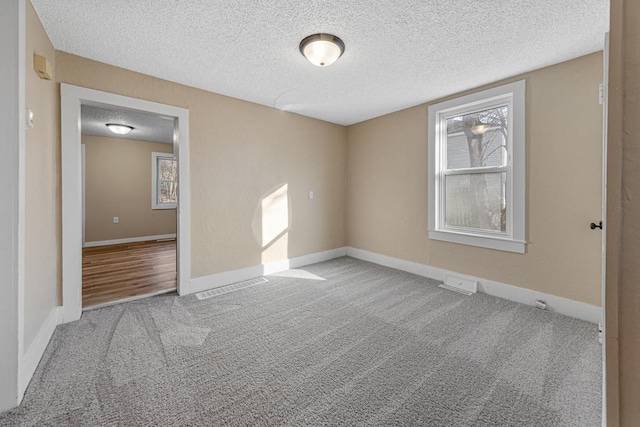 carpeted spare room featuring visible vents, a textured ceiling, and baseboards