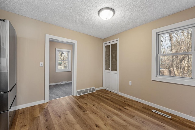 unfurnished room with baseboards, a textured ceiling, visible vents, and wood finished floors