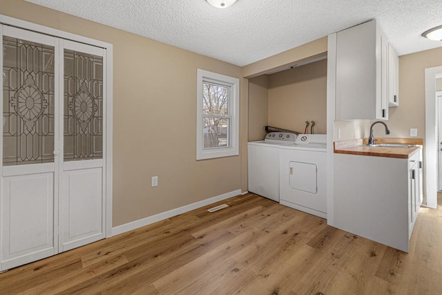 laundry area with light wood-style flooring, washing machine and dryer, a sink, a textured ceiling, and laundry area