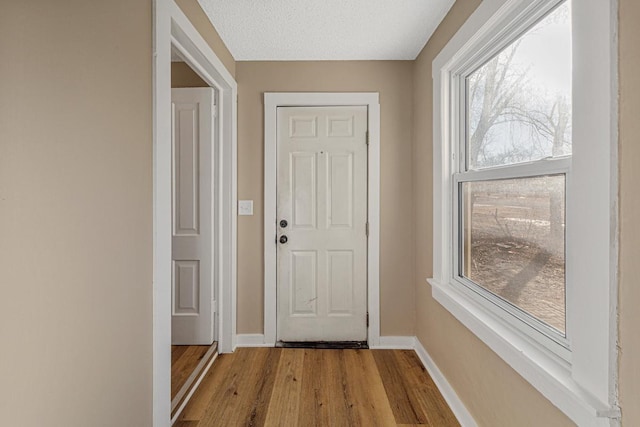 doorway featuring a textured ceiling, wood finished floors, and baseboards