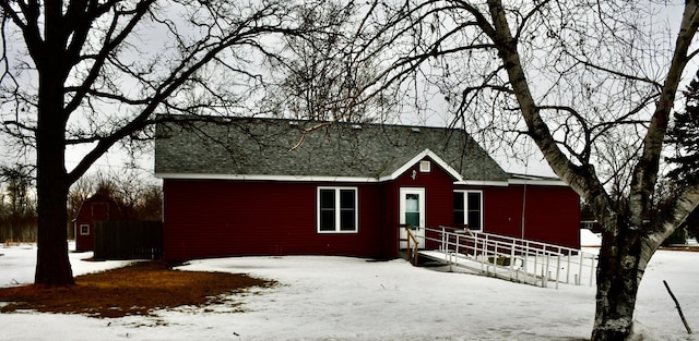 snow covered rear of property featuring a shingled roof