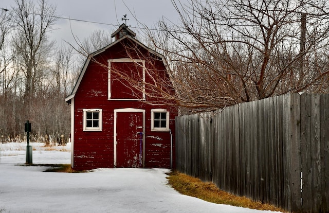 snow covered structure featuring a barn, fence, and an outdoor structure