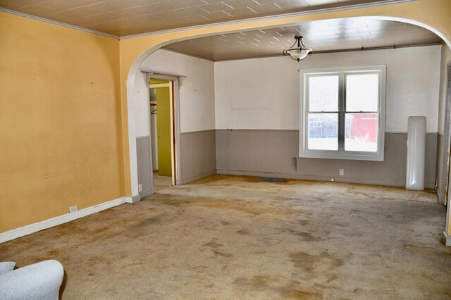 unfurnished room featuring baseboards, carpet, arched walkways, and crown molding