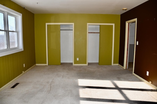 unfurnished bedroom with carpet, two closets, visible vents, and baseboards