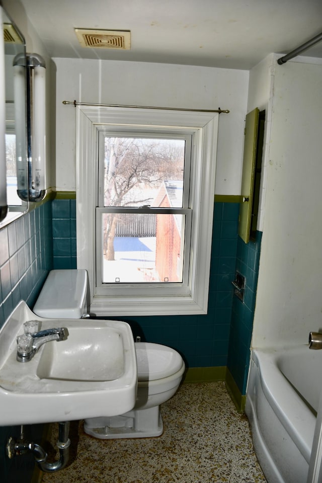 bathroom with visible vents, a wainscoted wall, a bathing tub, and tile walls