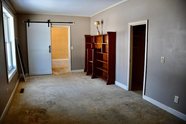 spare room featuring carpet floors, crown molding, visible vents, a barn door, and baseboards