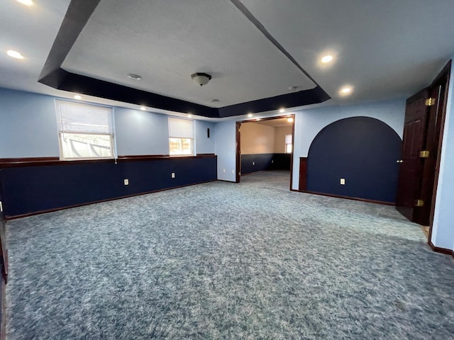 interior space featuring arched walkways, recessed lighting, baseboards, a tray ceiling, and carpet