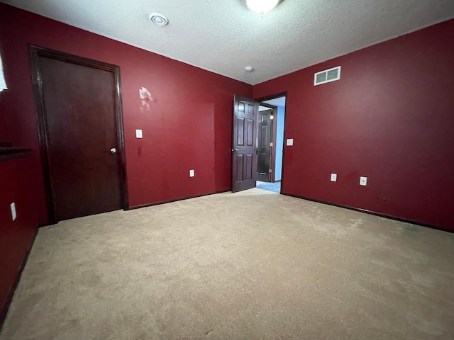 empty room with carpet, visible vents, and a textured ceiling