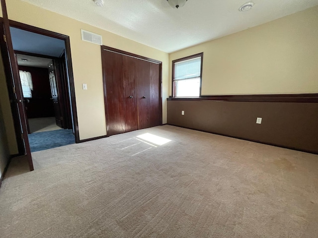 unfurnished bedroom with a closet, visible vents, light carpet, and baseboards