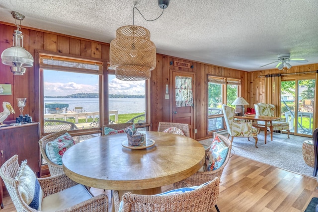 dining room with a water view, wood walls, light wood-style flooring, and a textured ceiling