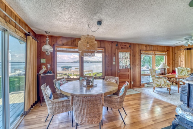 dining area with a textured ceiling, light wood-style flooring, and wooden walls