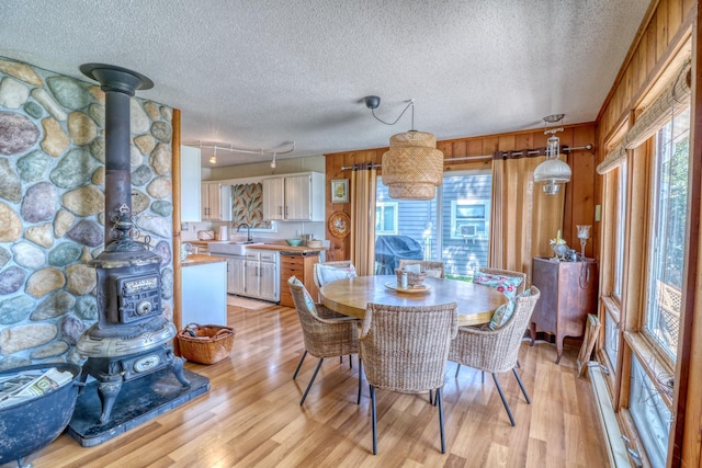 dining room with a textured ceiling, a wealth of natural light, light wood-type flooring, and a wood stove