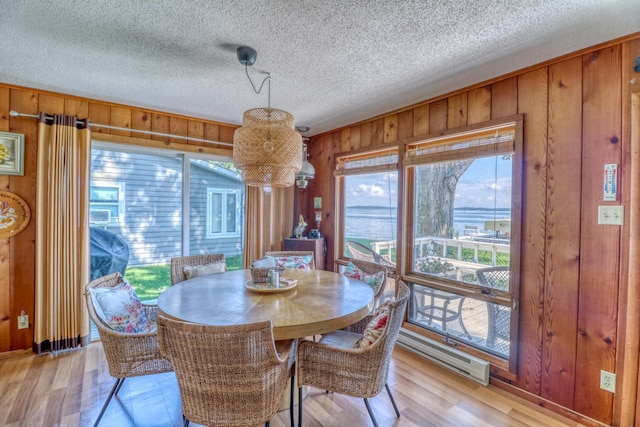 dining area with wooden walls, light wood finished floors, and a textured ceiling