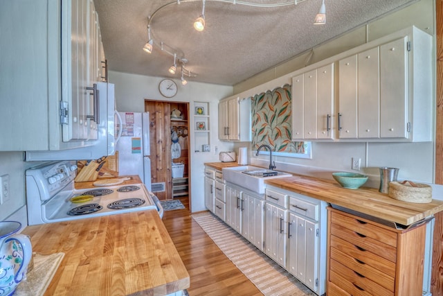 kitchen featuring light wood finished floors, wooden counters, white cabinetry, a sink, and white appliances