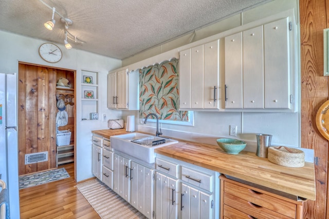 kitchen featuring a textured ceiling, butcher block counters, a sink, visible vents, and light wood-style floors