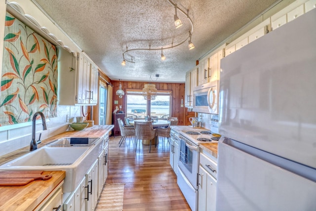 kitchen featuring white appliances, white cabinets, a textured ceiling, light wood-style floors, and a sink