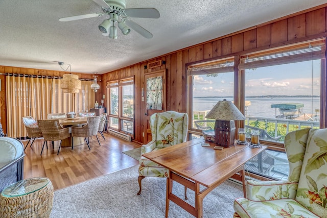 living room with a textured ceiling, ceiling fan, wood walls, a water view, and wood finished floors