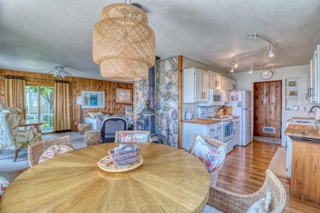 dining space with a ceiling fan, wood walls, a textured ceiling, and light wood finished floors