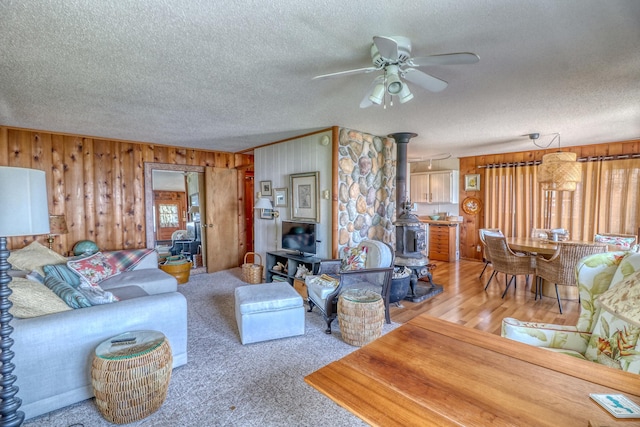 living area with a textured ceiling, ceiling fan, wood walls, and a wood stove