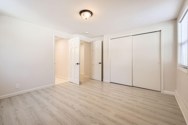 unfurnished bedroom with light wood finished floors, multiple windows, baseboards, and a closet