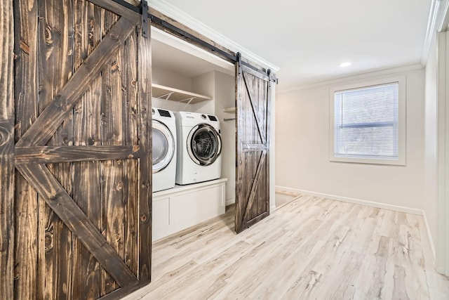 clothes washing area with laundry area, a barn door, washer and clothes dryer, and crown molding