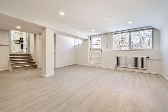 basement featuring recessed lighting, radiator, light wood-style floors, baseboards, and stairs