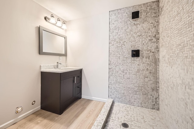 full bathroom with tiled shower, wood finished floors, vanity, and baseboards