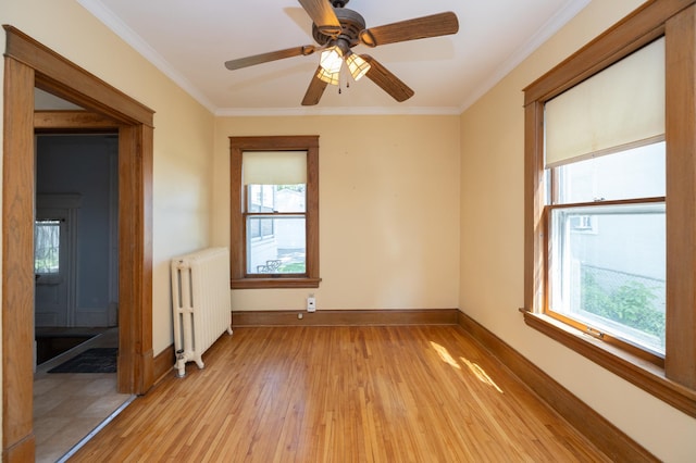 spare room featuring crown molding, radiator heating unit, light wood-style floors, a ceiling fan, and baseboards