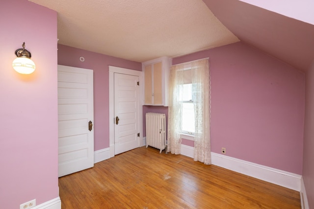 bonus room with radiator, vaulted ceiling, baseboards, and wood finished floors